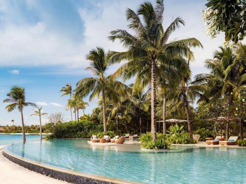 Duży basen z palmami i leżakami pod błękitnym niebem.