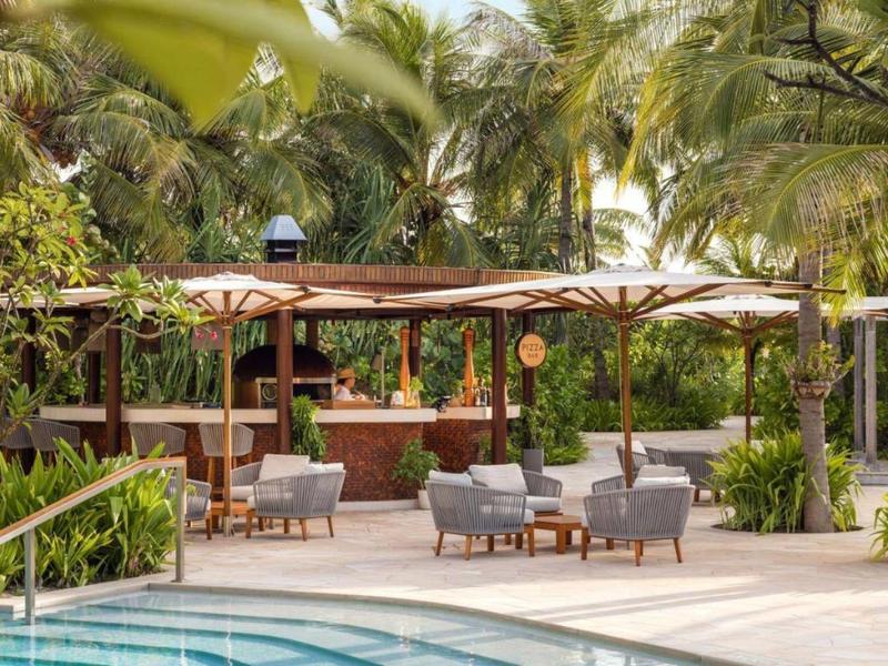 Strefa relaksu z fotelami i parasolami przy basenie otoczonym palmami.