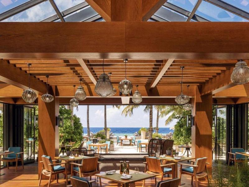 Otwarta jadalnia z drewnianymi belkami i widokiem na morze i basen.