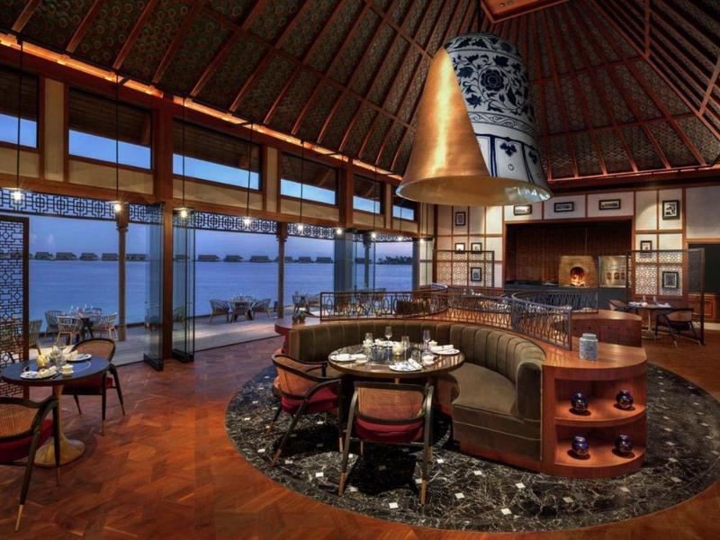 Elegancka restauracja hotelowa z panoramicznymi oknami i widokiem na wodę o zmierzchu.