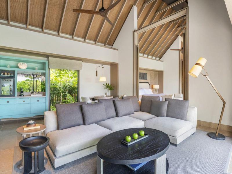 Jasny salon z szarą sofą, czarnym stołem i dużym lustrem na drewnianej ścianie.