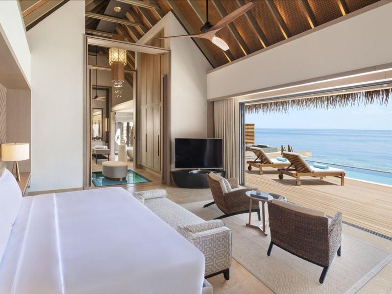 Jasny pokój hotelowy z widokiem na morze i tarasem z leżakami.