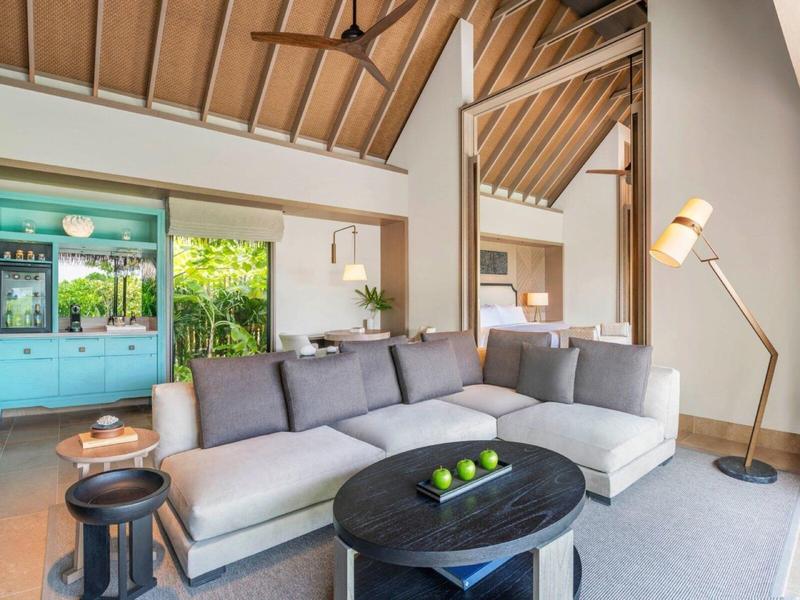 Jasny salon z szarą sofą, designerską lampą i dużą niebieską szafą przy oknach.