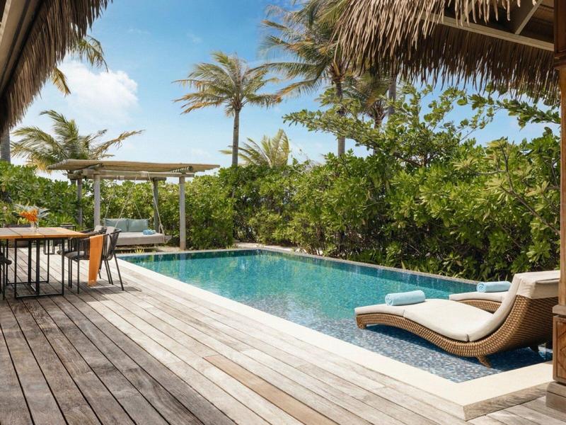 Nowoczesny basen z leżakami i drewnianym tarasem pod palmami i dachem ze słomy.