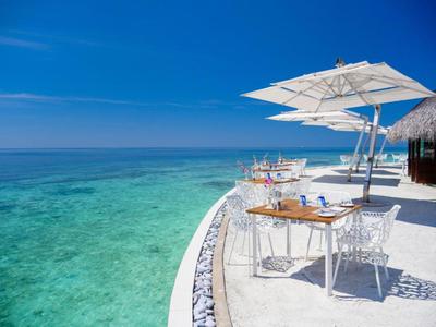 Restaurace pod širým nebem s bílými stoly a slunečníky u tyrkysového moře.