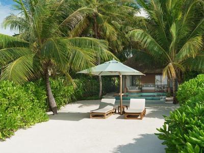 Deux chaises longues avec un parasol sur du sable blanc, entourées de palmiers et de plantes vertes.