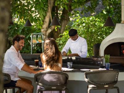 Couple profitant de boissons à un bar en plein air avec un barman et un grill en arrière-plan.