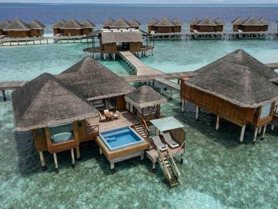 Bungalows sur pilotis avec piscine au-dessus d'eau turquoise claire dans un complexe tropical