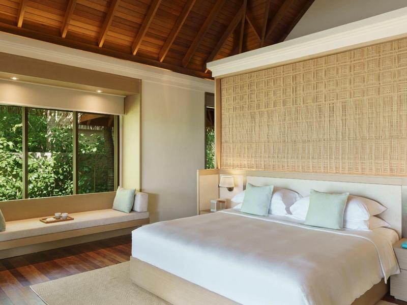 Chambre lumineuse avec grand lit, canapé-lit près de la fenêtre et plafond en bois.