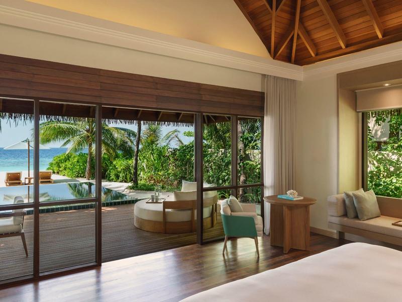 Chambre d'hôtel moderne avec vue sur terrasse, piscine et végétation tropicale.