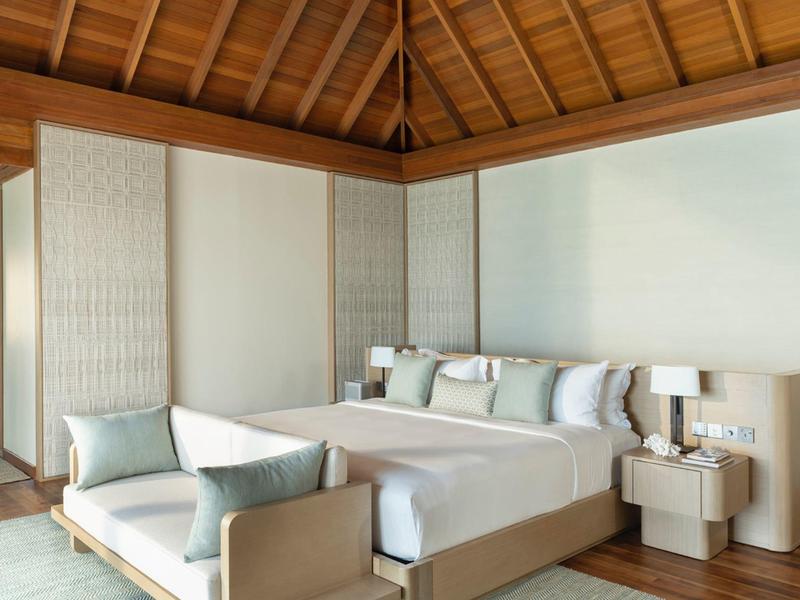 Chambre d'hôtel moderne avec plafond en bois, lit double, canapé et table de chevet aux tons neutres.