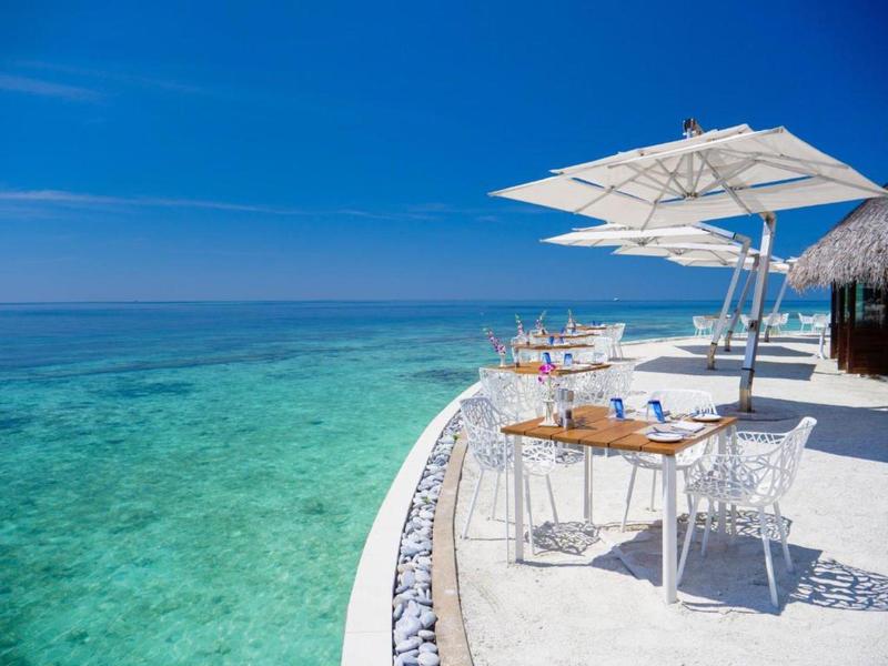 Terrasse avec tables et chaises blanches au bord de la mer turquoise sous un ciel bleu