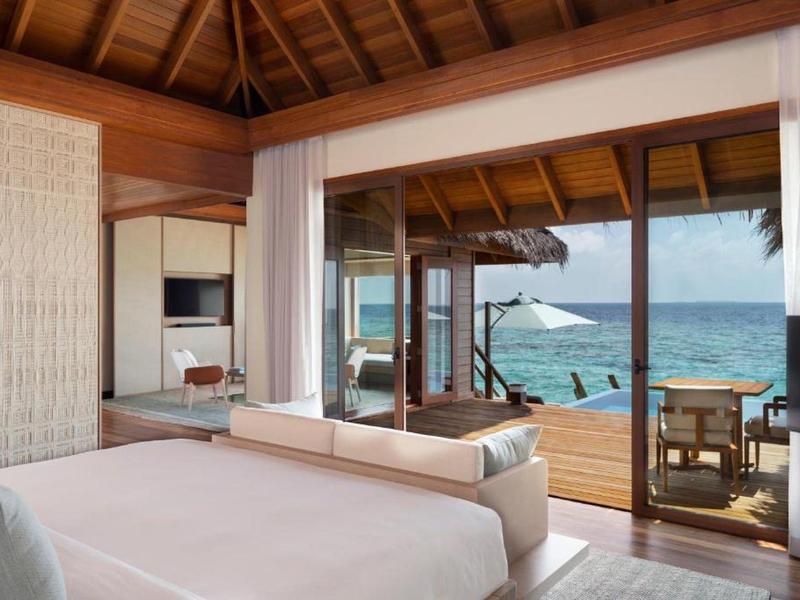 Chambre moderne avec vue sur la mer et accès à une terrasse en bois avec parasol.