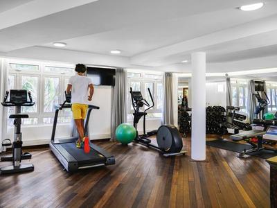 Moderner Fitnessraum mit Laufband, Crosstrainer, Hanteln und großem Spiegel an der Wand.
