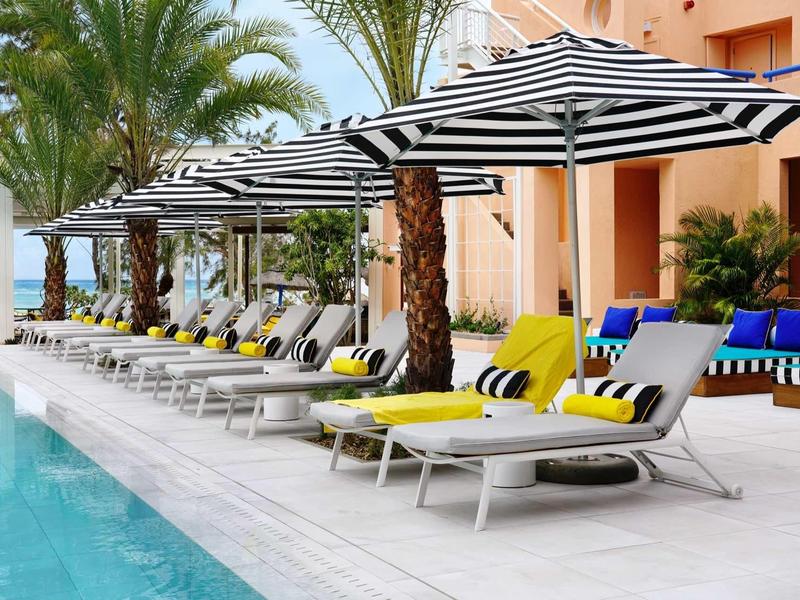 Swimmingpool neben Liegestühlen mit gelben Handtüchern und gestreiften Sonnenschirmen.