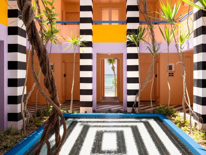 Innenhof mit schwarz-weiß gestreiften Säulen, bunten Wänden und einem quadratischen Gartenbeet.