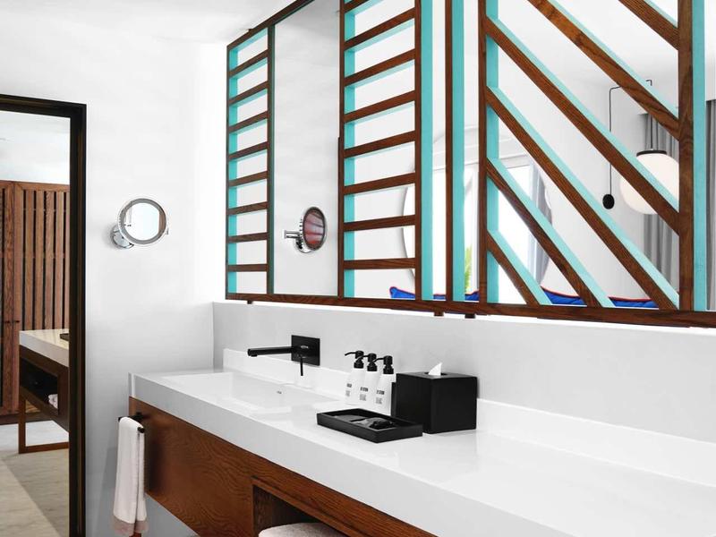 Modernes Badezimmer mit langem weißen Waschtisch und dekorativen Holzfenstern in einem Hotelzimmer.