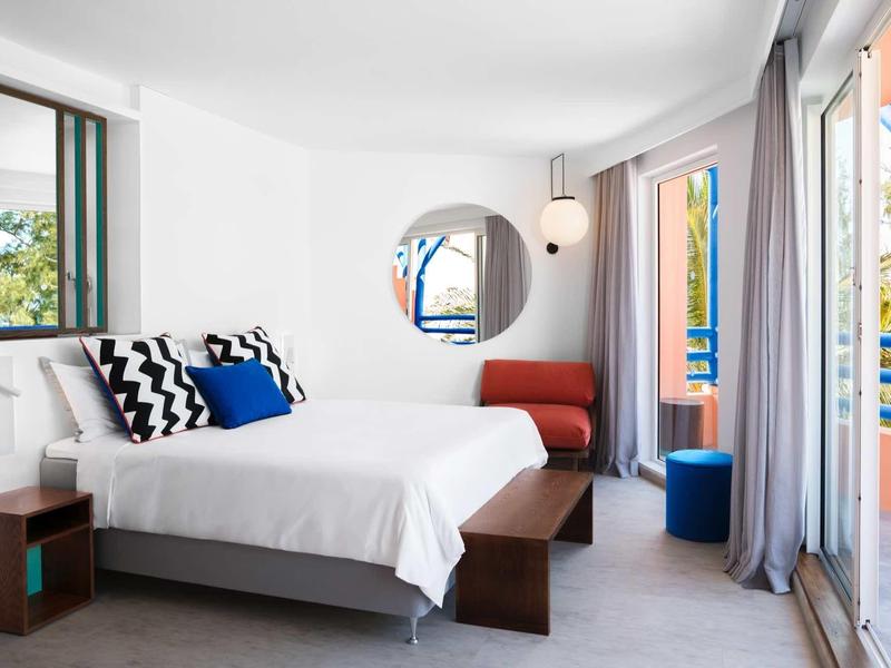 Helles Hotelzimmer mit Doppelbett, modernen Möbeln und Balkon mit Blick ins Grüne.