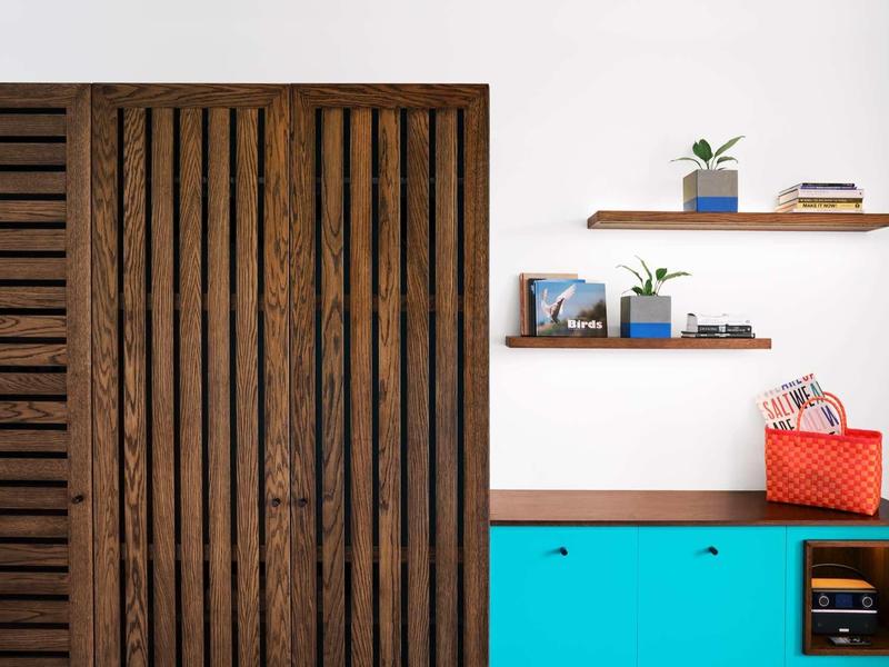 Moderner Raum mit hölzernen Schiebetüren, blauer Kommode und Regalen mit Pflanzen und Büchern.