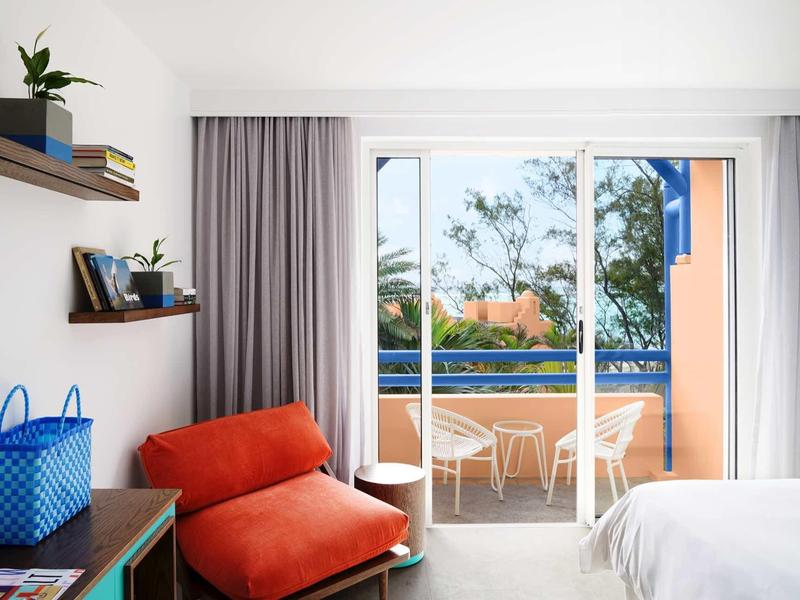 Modernes Hotelzimmer mit rotem Sessel und Terrasse mit Blick auf Pool und Bäume.