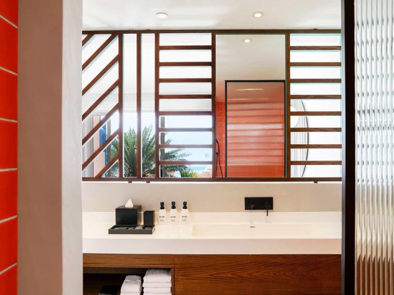 Modernes Badezimmer mit großer Spiegelwand, Holzdetails und rotem Akzent an der Wand.