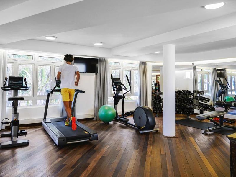 Moderner Fitnessraum mit Laufband, Crosstrainer, Hanteln und großem Spiegel an der Wand.