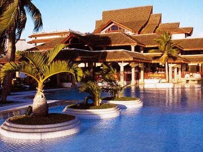 Gran piscina frente a un hotel tropical tradicional con palmeras y cielo azul.