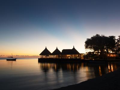 Dämmerungsblick auf ein Resort am Wasser mit hölzernen Hütten auf Pfählen und Boot.