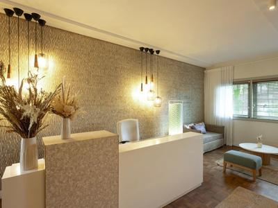 Moderne Empfangstheke mit hängenden Lampen, Trockenblumen und Sitzbereich mit Sofa und Hocker.