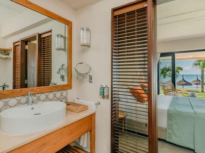 Modernes Badezimmer mit rundem Waschbecken, Holzablage und Tür zu Schlafzimmer mit Meerblick.