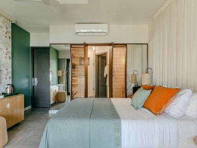 Modernes Hotelzimmer mit Doppelbett, grauer Bettdecke, orangenen Kissen und begehbarem Kleiderschrank.