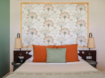 Gemütliches Hotelzimmer mit Doppelbett, orangegrünen Kissen und gemustertem Kopfteiler.