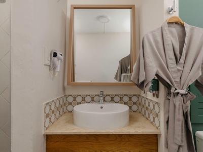 Moderner Badezimmerbereich mit weißem Waschbecken, Holzablage, dekorativem Fliesenspiegel und Bademantel an der Wand.