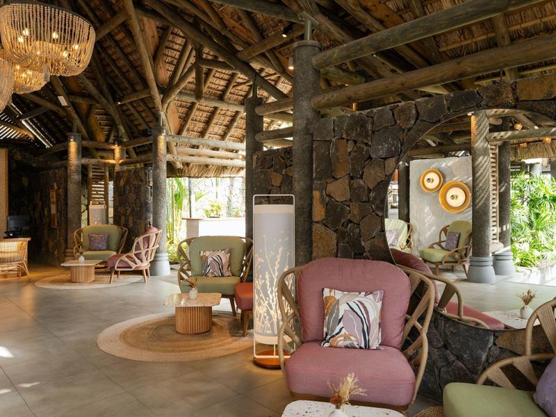 Rustikales Wohnzimmer mit Holzdecke, Steinwänden, lila Sesseln und großen Fenstern, viel Tageslicht.