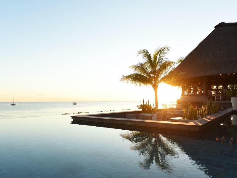 Sonnenuntergang am Infinity-Pool mit Palmen, offenem Dach und ruhigem Meer im Hintergrund.