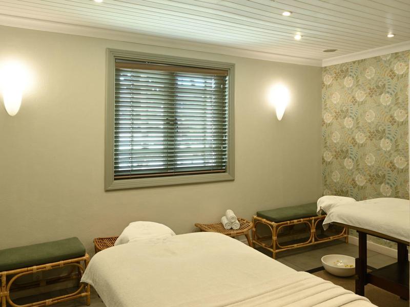 Ein ruhiger Raum mit zwei Massageliegen, grünen Polsterbänken und gedämpfter Beleuchtung.