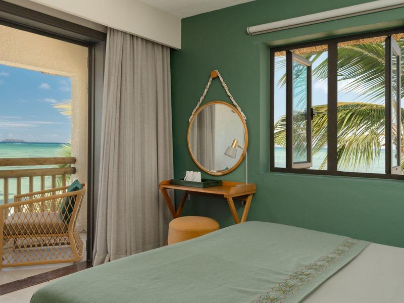 Schlafzimmer mit grüner Wand, Spiegel, Schminktisch und Blick auf Balkon mit Meerblick.