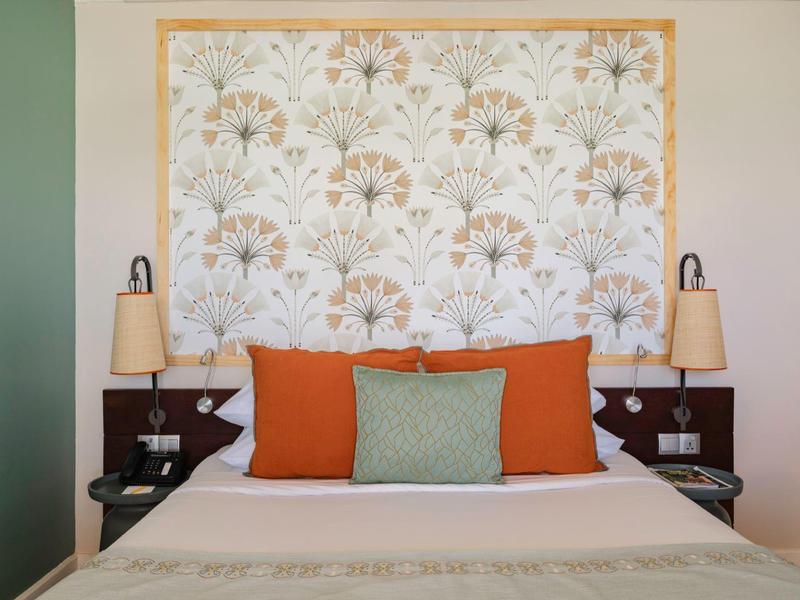 Gemütliches Hotelzimmer mit Doppelbett, orangegrünen Kissen und gemustertem Kopfteiler.