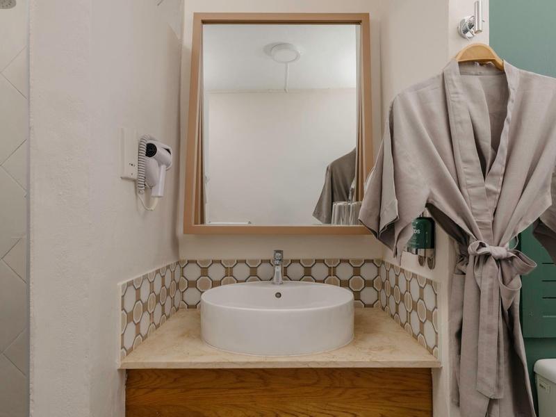 Moderner Badezimmerbereich mit weißem Waschbecken, Holzablage, dekorativem Fliesenspiegel und Bademantel an der Wand.