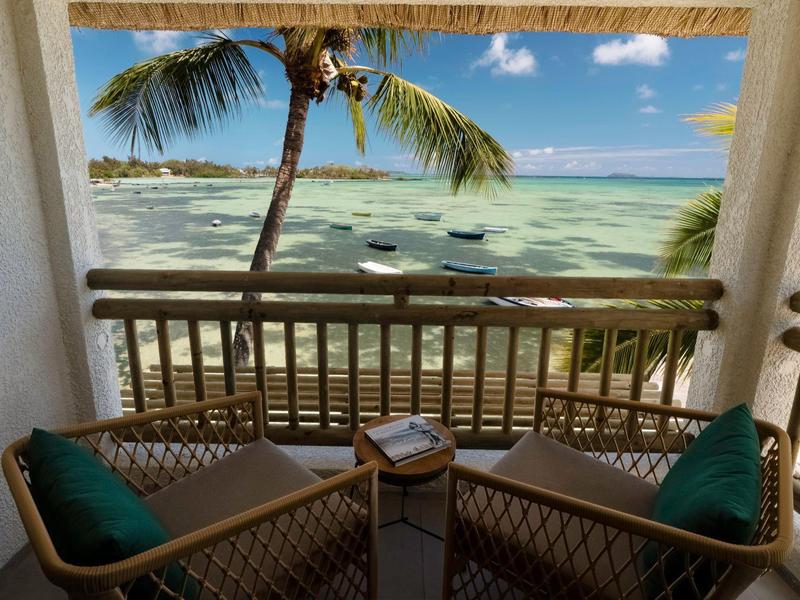 Balkon mit zwei Stühlen, Tisch und Blick auf Palmen und das Meer bei klarem Wetter.