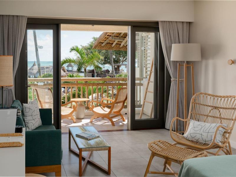 Helle Hotelzimmer mit Korbsessel, Sofa und Terrasse mit Blick auf Palmen und Meer