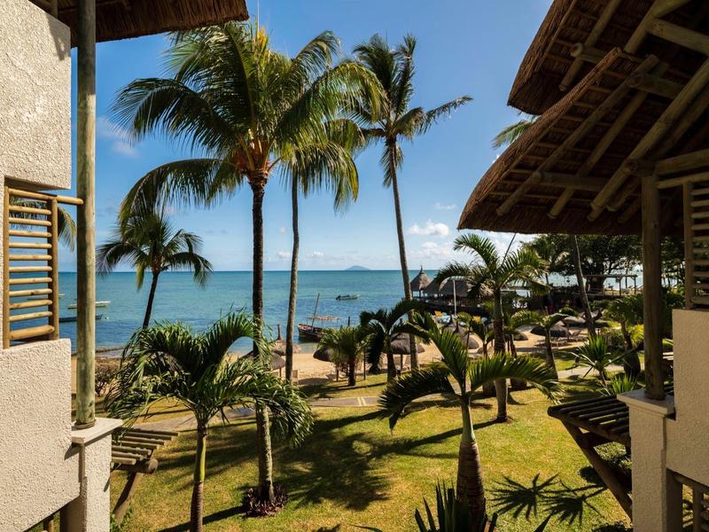 Blick auf einen tropischen Garten mit Palmen und Meer vom Balkon eines Hotels.