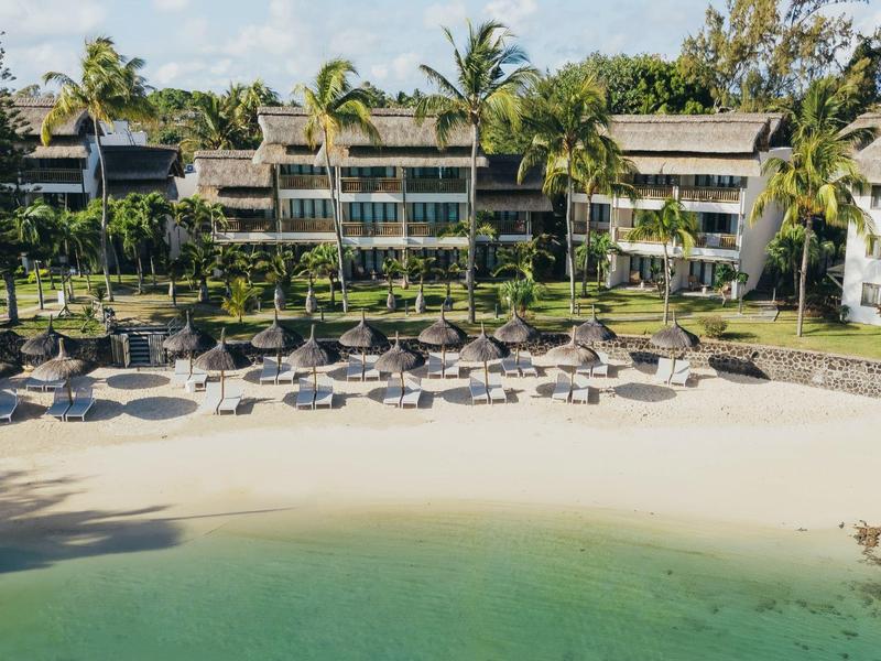 Strand mit weißem Sand, Liegen, Palmen und mehrstöckigen Gebäuden im Hintergrund.