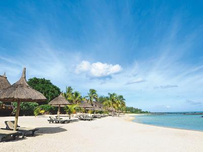 Plage de sable blanc avec des huttes en chaume et des chaises longues sous un ciel bleu au bord de la mer