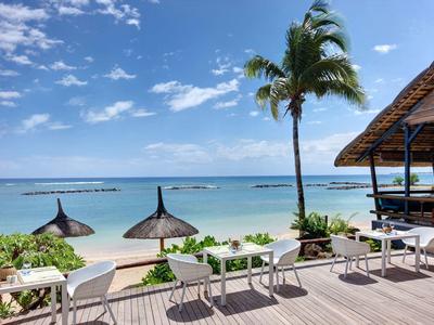 Terrasse avec tables et chaises donnant sur des palmiers, une plage de sable et la mer sous un ciel bleu.