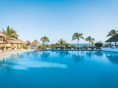 Großer Pool mit Liegestühlen, Palmen und Restaurant am Meer bei klarem Himmel.