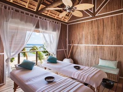 Une salle de spa lumineuse avec deux tables de massage, des rideaux et une vue sur la mer.