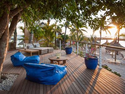 Terrasse avec poufs, canapés et plantes avec vue sur la mer au coucher du soleil.