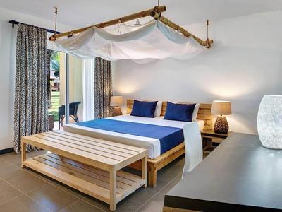 Chambre d'hôtel moderne avec grand lit, banc en bois, lampe et rideaux à la fenêtre.