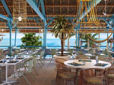 Offenes Strandrestaurant mit Holzdach, Rattanmöbeln und Blick auf das Meer bei Tageslicht.